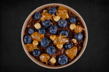 Delicious healthy breakfast with Whole oats, oat milk, chia seeds, cocoa, hazelnuts, natural peanut butter, fresh blueberries and honey on black background