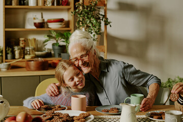 Portrait of elderly man enthusiastically baking cookies with young granddaughter in cozy kitchen. Both sharing moment of happiness and bonding over homemade treats