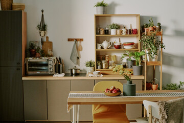 Compact and inviting kitchen setup highlighting sleek cabinets, shelving with assorted kitchenware, and variety of potted plants. Wooden table and chairs adding warmth and charm