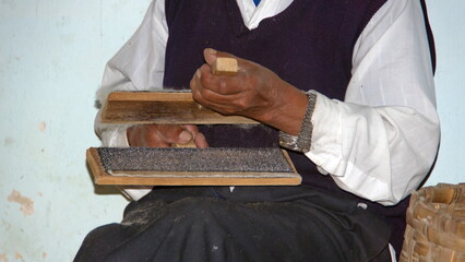 Hands of an elderly, indigenous man carding wool in an artisan's workshop in Carabuela, Ecuador