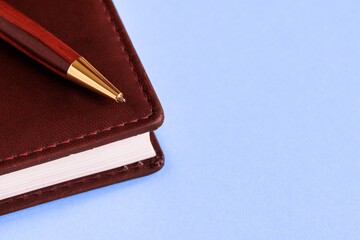 A diary in brown leather and a fountain pen on a blue background. Business concept.