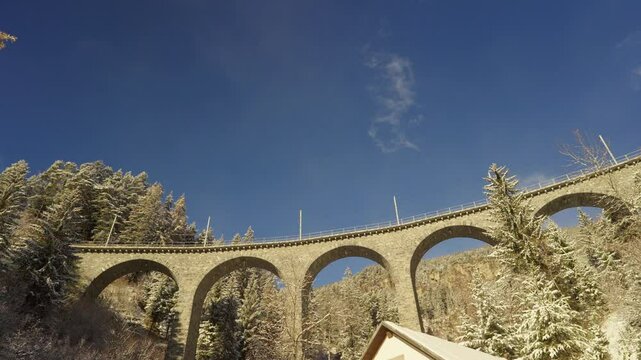 Train crossing famous Schmittentobel Viaduct of RHB narrow gauge railway at Swiss mountain village of Schmitten on a snowy autumn day. Movie shot November 22nd, 2024, Schmitten, Switzerland.
