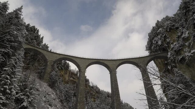 Train crossing famous Landwasser Viaduct of RHB narrow gauge railway at Swiss mountain village of Filisur on a snowy autumn day. Movie shot November 22nd, 2024, Filisur, Switzerland.