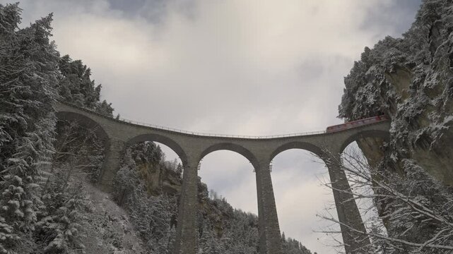 Train crossing famous Landwasser Viaduct of RHB narrow gauge railway at Swiss mountain village of Filisur on a snowy autumn day. Movie shot November 22nd, 2024, Filisur, Switzerland.
