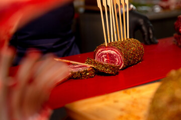 Beef roulade with herbs and kitchen sticks and two slices cut on a red table in a butcher shop. Barbecue preps seasoned with pepper mix. Cooking conept.