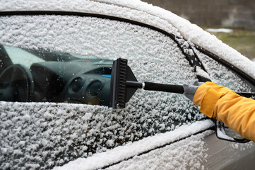 Driver is removing snow from car windshield with ice scraper and broom, clean car window from icy...