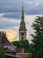 Fototapeta premium A historic church spire pierces through a dramatic, cloudy sky. The image captures the timeless beauty of London's architecture against the ever-changing backdrop of nature.