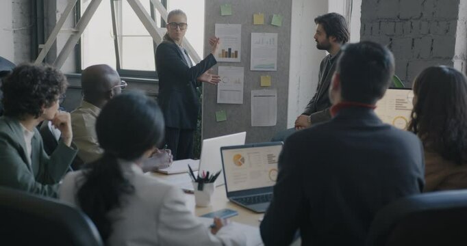 Young businesswoman presenting successful solution at team meeting while colleagues clapping hands in office. Professional accomplishment and people concept.