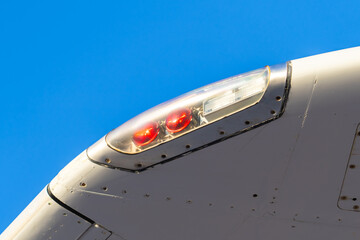 Close-up view of an aircraft wingtip highlighting navigation lights against a clear blue sky during daytime