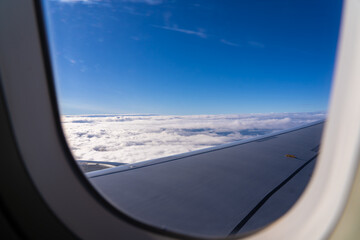 Cloudy sky viewed from an airplane window reveals a vast blue horizon and fluffy white clouds during a sunny flight