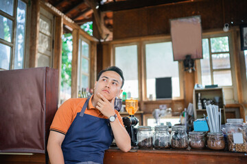handsome barista in apron waiting customer with hand on chin gesture