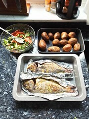 Two perfectly grilled fish lay on crinkled aluminum foil in a kitchen. The setting highlights the care taken in cooking and presentation, emphasizing a delicious meal