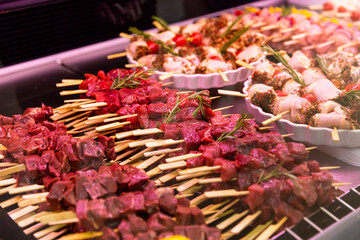Beef meat and raw chicken rolls seasoned with mixed peppers and rosemery on skewers. Diverse raw meat products for sale.