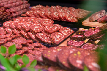 Different assortment of meat and row beef roll with herbs and kitchen sticks on window shop. Diverse raw meat products for sale.
