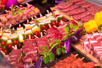 Row beef burger cutlets and lamb meat for grilled raw meat products seasoned with mixed peppers and rosemery on skewers. Diverse raw meat products for sale.