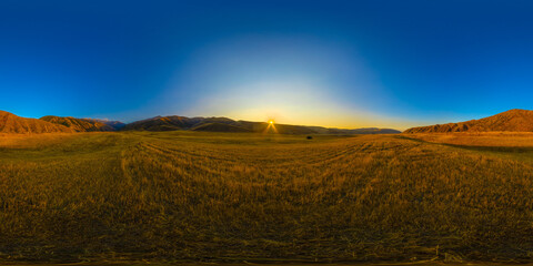 Fototapeta premium Full Spherical panorama of straw moved agricultural field surrounded with foothills at autumn sunset with blue sky in equirectangular projection