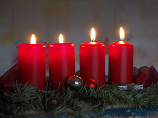 Blick auf ein Adventsgesteck mit grünen Tannenzweigen und Christbaumkugeln, vier rote Kerzen brennen darauf, 