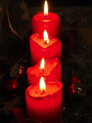 Weihnachtliche Stimmung mit vier roten Kerzen, die hintereinander auf einem Adventsgesteck stehen, ihr Licht leuchtet in der Dunkelheit, 