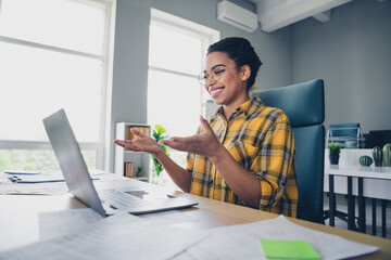 Photo of lovely young lady talking presentation video call netbook dressed yellow plaid shirt comfortable startup office loft room interior