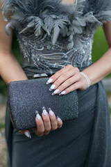 Close-up of a woman wearing a formal  gray dress, her hands with an attractive manicure, holding a glittering handbag. Selective focus.