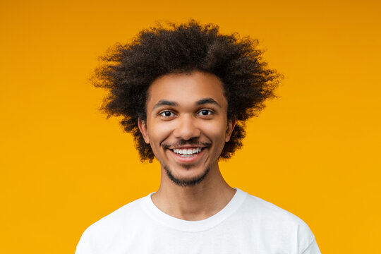Close up studio portrait of young handsome African American man in plain white t-shirt posing over yellow background