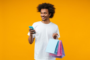Portrait of attractive smiling African American young man with shopping bags in hand using his...