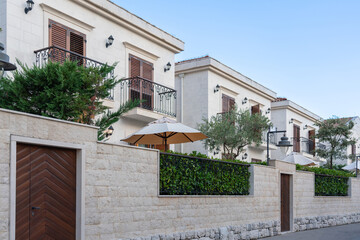 A row of elegant modern villas with balconies and lush greenery, enclosed by a stone wall, showcasing upscale residential living.