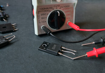 A power transistor on the bench with the multimeter. Focused on the being tested component.