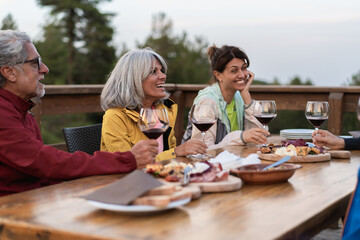 Friends enjoying wine tasting with charcuterie board during outdoor gathering with authentic laughter