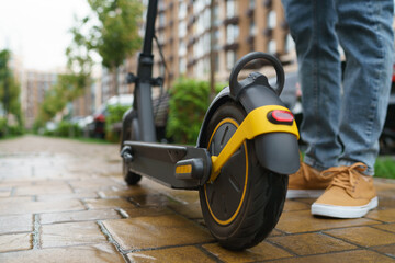 Close up cropped low angle shot of the feet of unrecognizable man standing by electric kick scooter e-scooter outdoors with the street square or park on the background