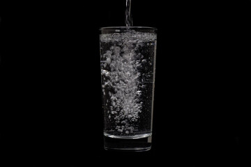 Image of water pouring into glass on black background.