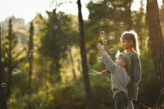 a boy and a girl are walking in the forest and blowing soap bubbles - Powered by Adobe