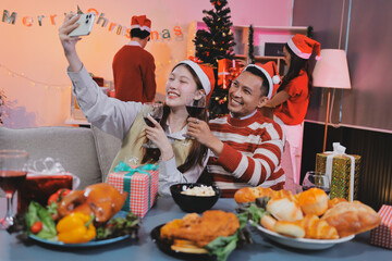 Group of happy Asian friends celebrating Christmas and decorate the Christmas tree indoors. Beauty woman with Christmas Gifts. New Year party. Woman hands decorate Christmas tree red ball, bauble.