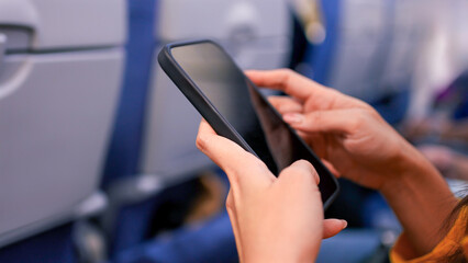 A closeup of woman hands holding a smartphone inside an airplane. Modern travel.