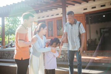 asian grandfather greeting his grandchild and her parent by hand shake