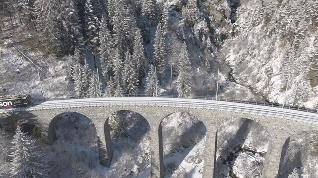 Aerial view of train crossing famous Schmittentobel Viaduct of RHB narrow gauge railway at Swiss mountain village of Schmitten on an autumn day. Movie shot November 22nd, 2024, Schmitten, Switzerland.