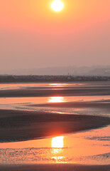 romantic background of yellow orange sun and the reflection of sunlight on the wet sand at the...