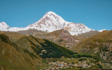 Gergeti Trinity Church perched on a hill with the snow-covered Mount Kazbek towering in the background, under a vibrant blue sky in Georgia