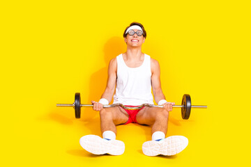 Energetic young man in activewear seated on vibrant yellow background with barbell, embodying healthy lifestyle and fitness motivation