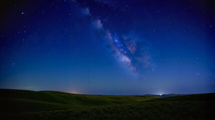 Starry night sky over a grassy hill