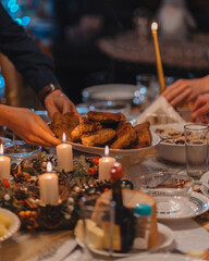 Christmas Supper. People serving dishes to each other. On the set table fish, candles, wreath. A warm Christmas atmosphere.