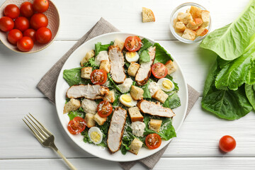 Tasty Caesar salad with chicken and tomatoes on white wooden table, flat lay