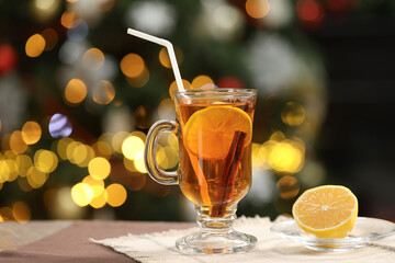 Hot tea with lemon and cinnamon on table against blurred Christmas lights, space for text. Bokeh effect