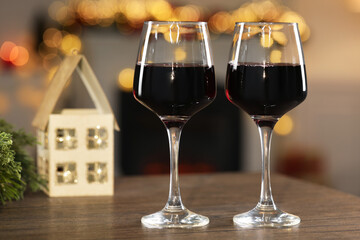 Red wine in glasses on wooden table against blurred Christmas lights, bokeh effect