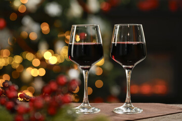 Red wine in glasses on table against blurred Christmas lights, space for text. Bokeh effect