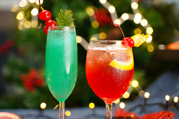 Vibrant green and red festive cocktails garnished with cherries and citrus slices, set against a backdrop of holiday lights and Christmas decorations.