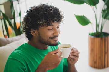 Portrait of nice young man closed eyes smell coffee wear t-shirt modern green interior flat indoors