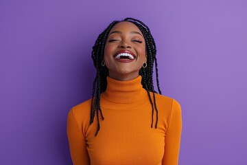 Joyful woman in orange sweater with braided hair against purple wall
