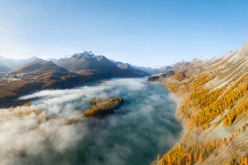 Obraz premium Drone view of a mountain valley with fog. Engadin valley, Switzerland. Autumn landscape from the air. Sun rays in the mountains. Photo for background, wallpaper, postcards.