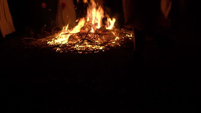 Unrecognizable people dance circle around a big campfire at night. View people legs 4K